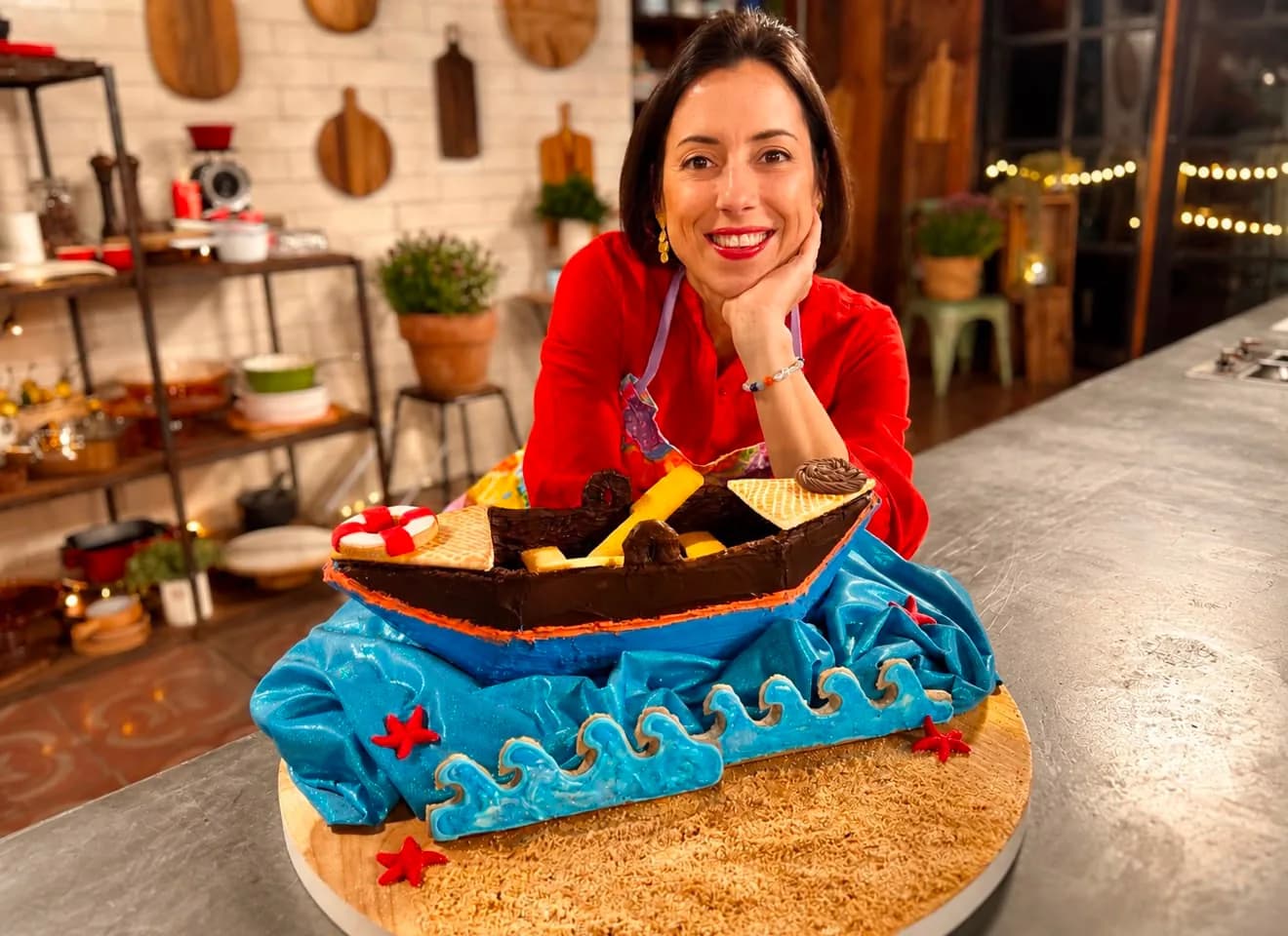 Pam holding a chocolate boat cake set on blue buttercream waves