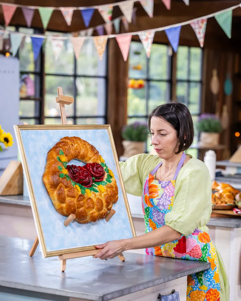 Pam on the set of The Great Australian Bake Off, placing her braided bread wreath on an easel